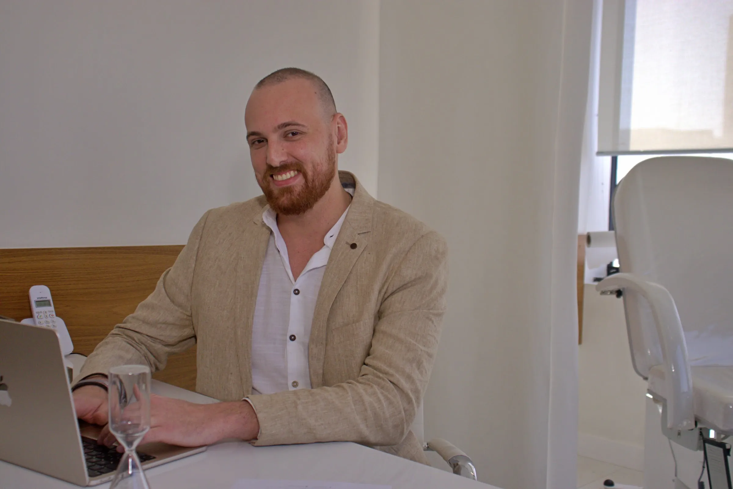 Dr. Guilherme Leitner sorrindo à mesa do consultório, com o computador aberto